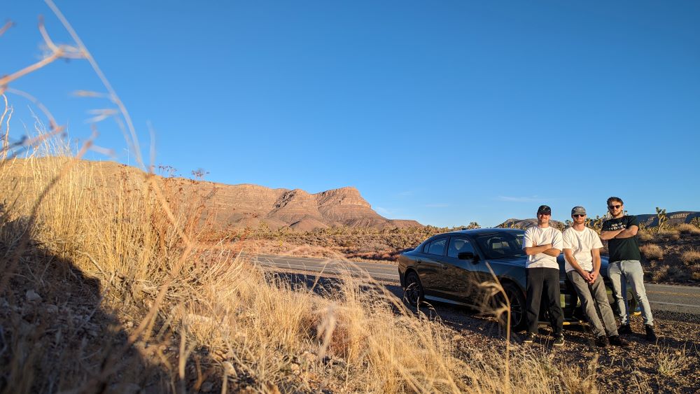 Jack and 2 friends in front of a car on a highway in the desert