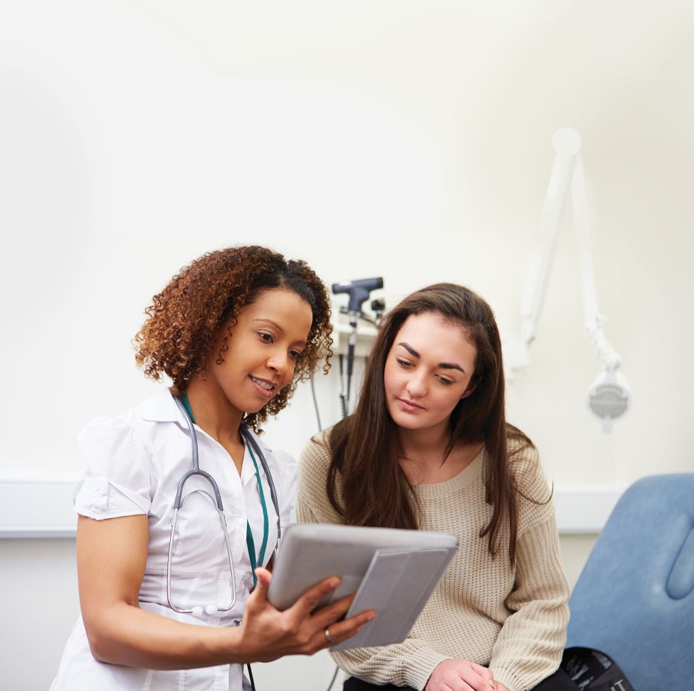 Nurse talking to young woman and showing her an ipad